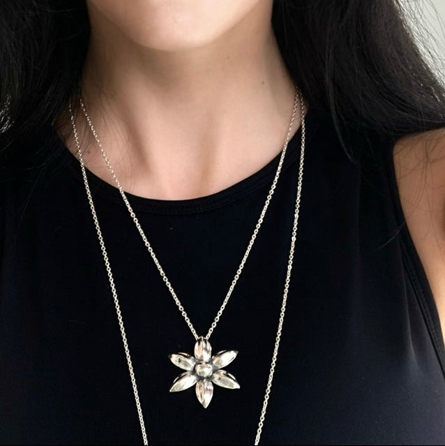 Close-up of a person wearing a silver necklace with a floral pendant on a black background