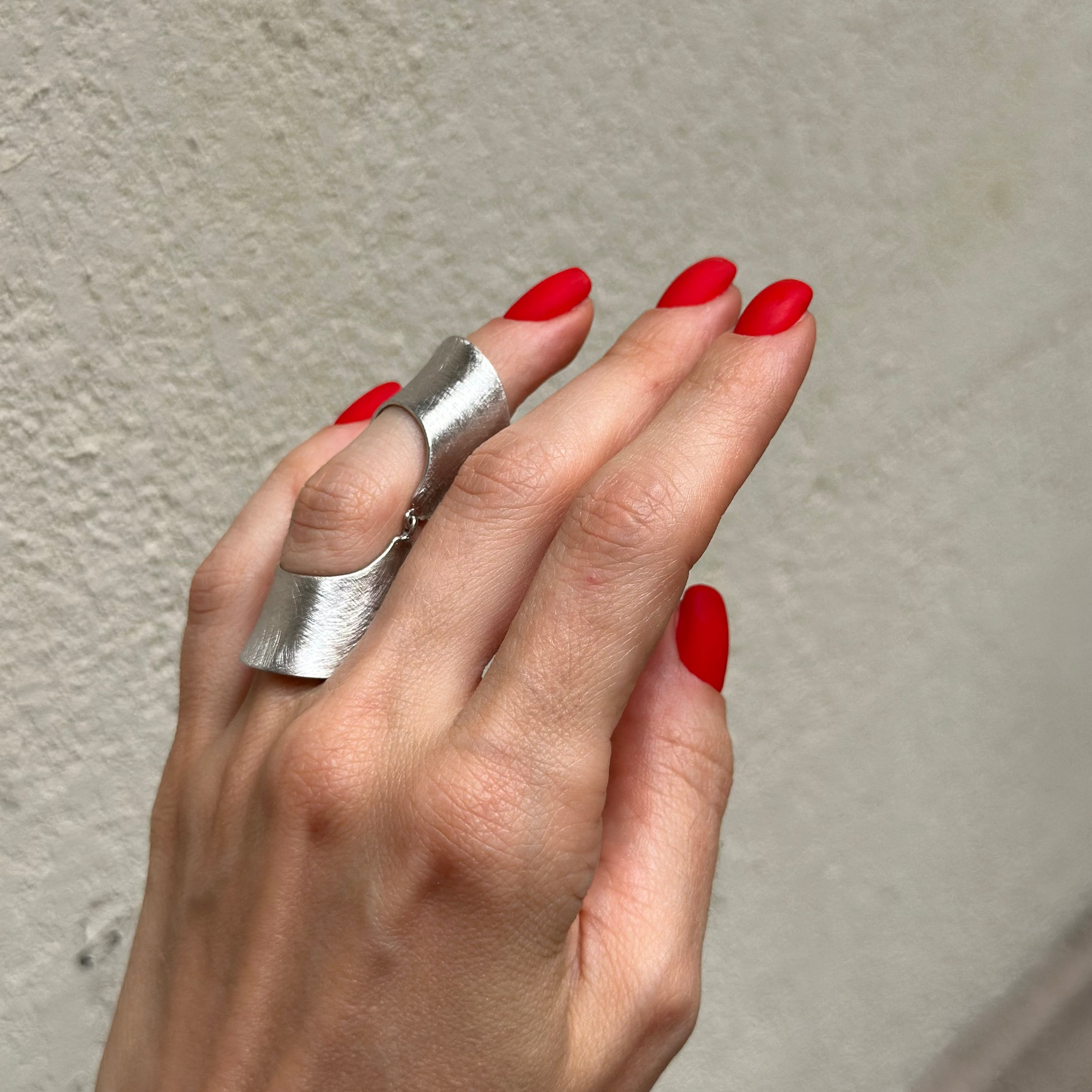 Hand with silver ring and red nails against a textured wall.